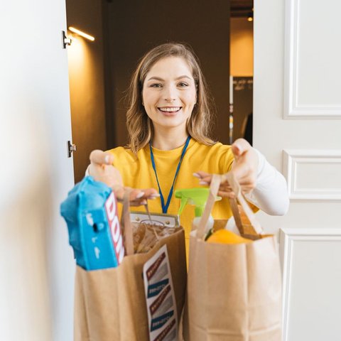 Smiling woman in a doorway holding two paper bags of groceries